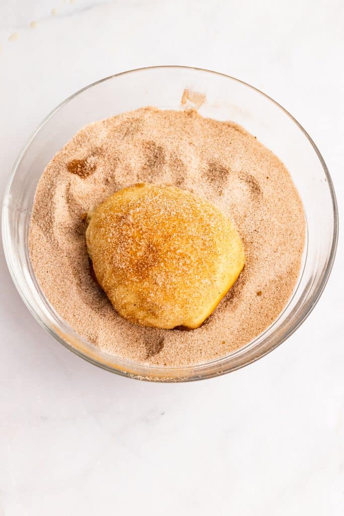 baked apple pie bomb in a bowl of cinnamon sugar