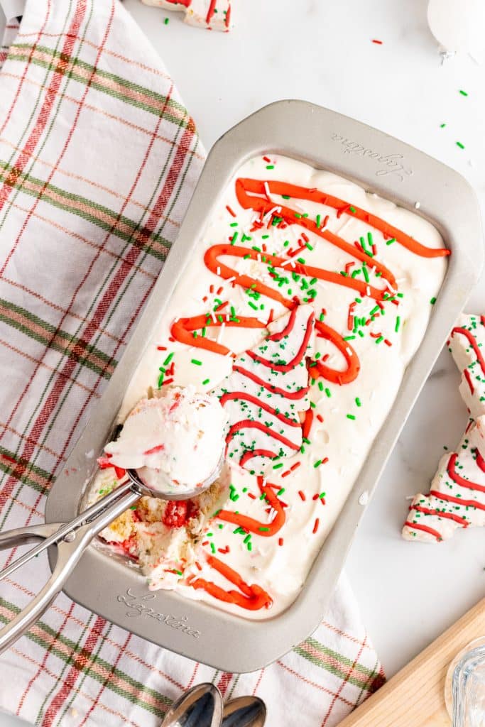 a metal scoop full of christmas tree cake ice cream resting on a metal loaf pan