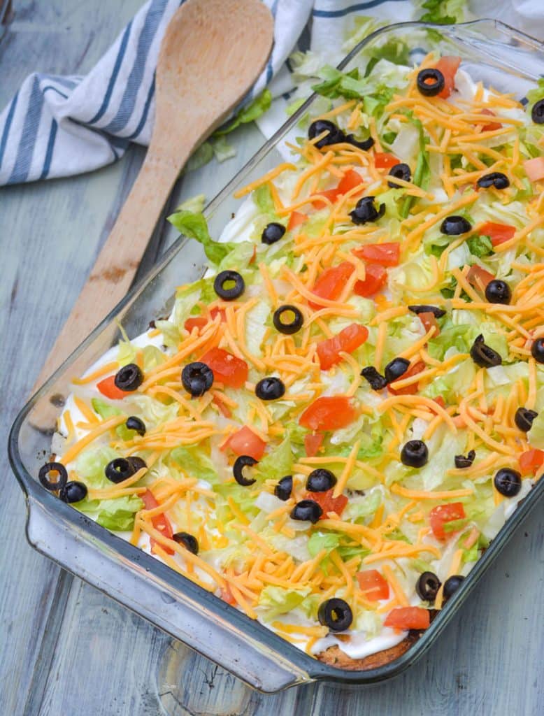 bisquick taco bake in a pyrex baking dish topped with shredded lettuce, diced tomatoes, cheese, and sliced olives
