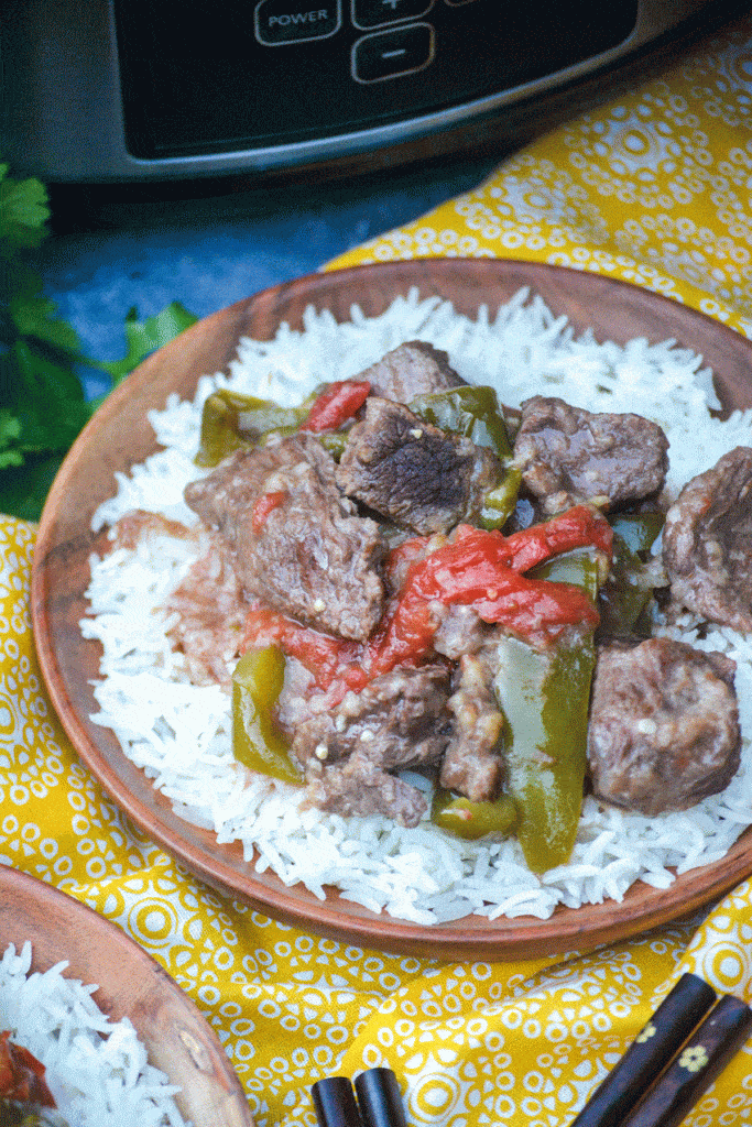 crockpot pepper steak over a bed of steamed white rice on a wooden plate