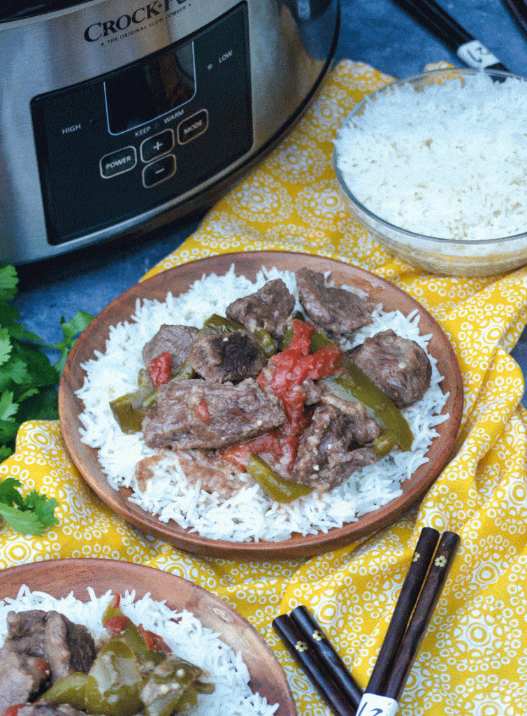 crockpot pepper steak over a bed of steamed white rice on a wooden plate