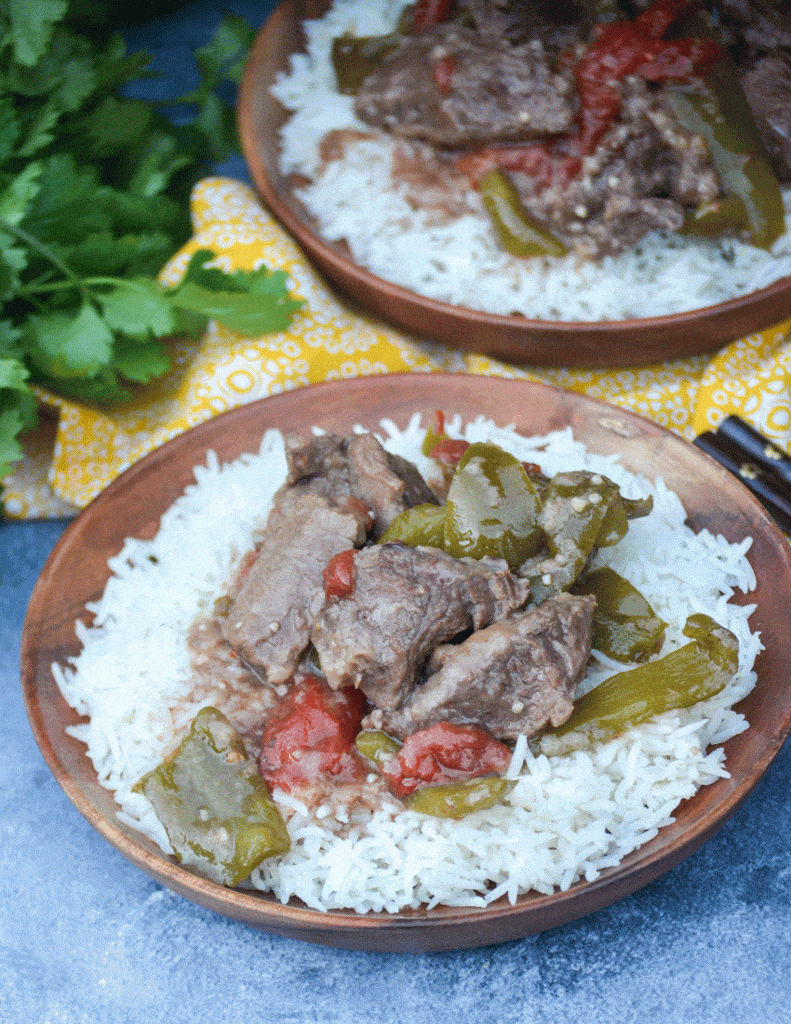 crockpot pepper steak over a bed of steamed white rice on a wooden plate
