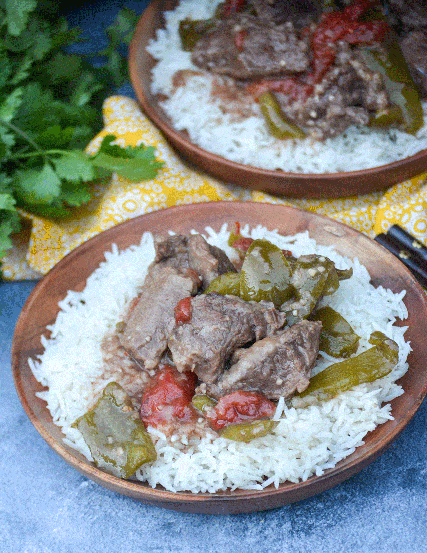 crockpot pepper steak over a bed of steamed white rice on a wooden plate