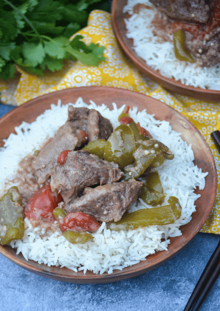 crockpot pepper steak over a bed of steamed white rice on a wooden plate