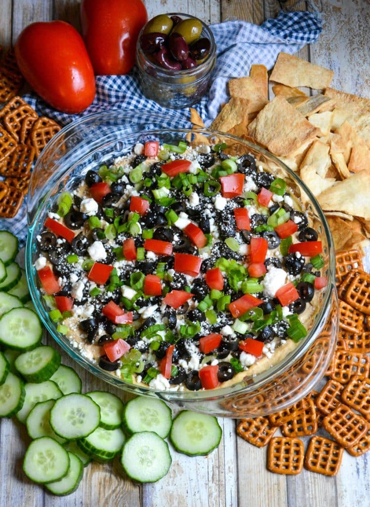 7 layer Greek dip in a glass pie pan surrounded by crackers and pretzels