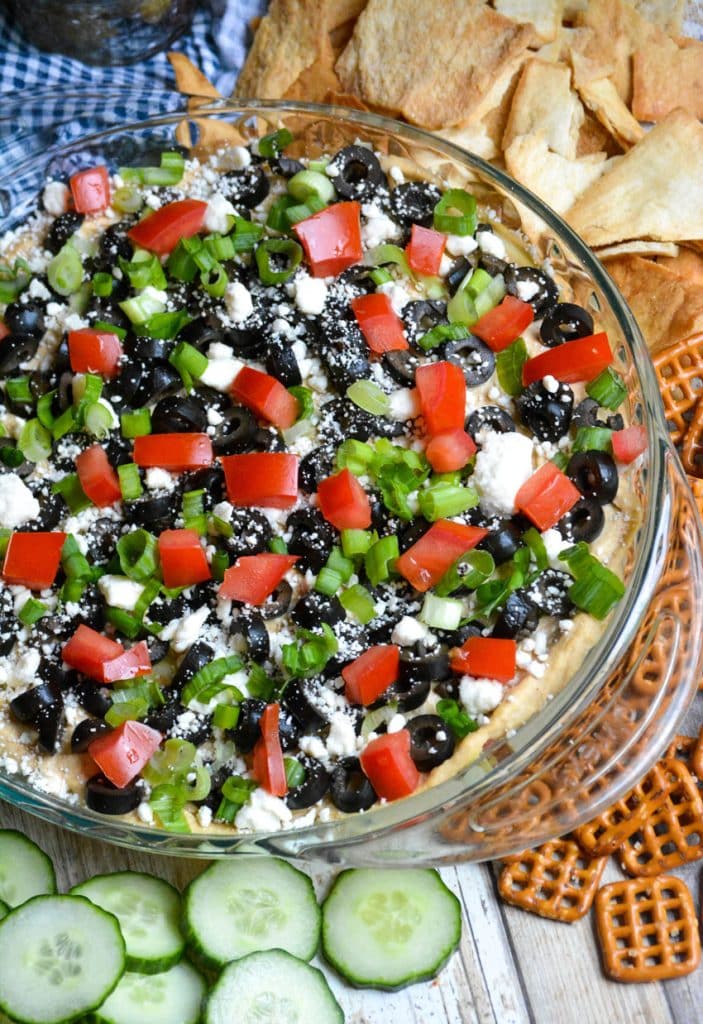 7 layer Greek dip in a glass pie pan surrounded by crackers and pretzels