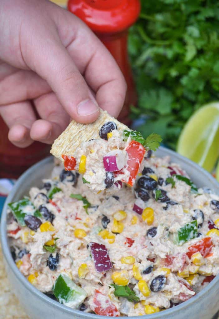 a small hand holding up a square cracker topped with mexican tuna salad