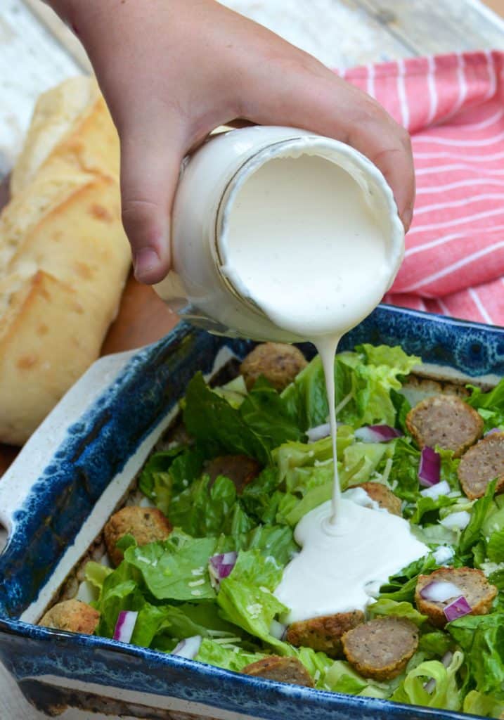simple cream salad dressing being poured from a jar over a bed of lettuce