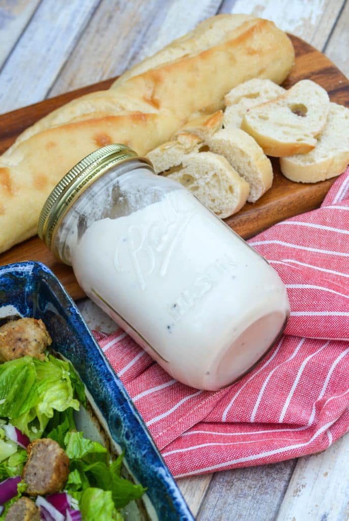 a glass mason jar filled with cream salad dressing lying on its side on a red cloth napkin