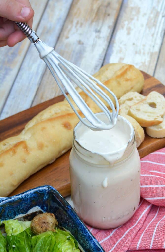 a whisk covered in cream salad dressing held above a glass mason jar