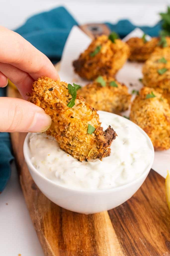 a hand dipping an air fryer fish stick into a white bowl of tartar sauce