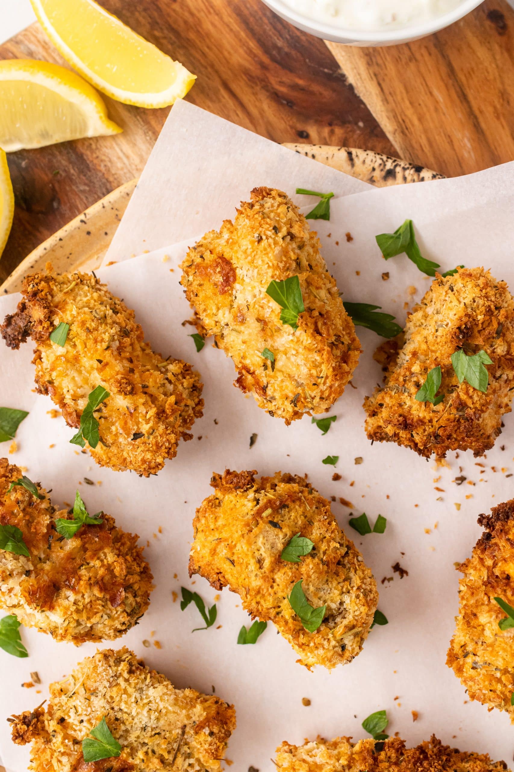 air fryer fish sticks on a parchment paper covered cutting board with fresh herbs and lemon wedges
