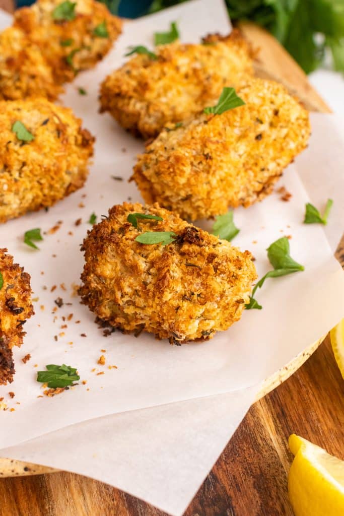 air fryer fish sticks on a parchment paper covered cutting board with fresh herbs and lemon wedges