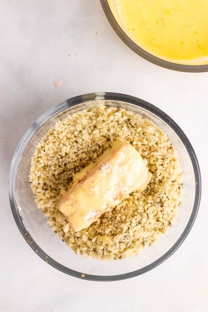 egg washed piece of cod resting in a bowl of seasoned panko bread crumbs