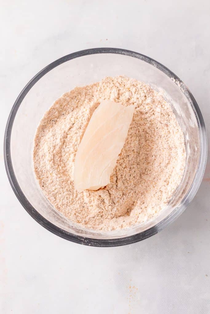 thin piece of raw cod sitting in a bowl of seasoned flour