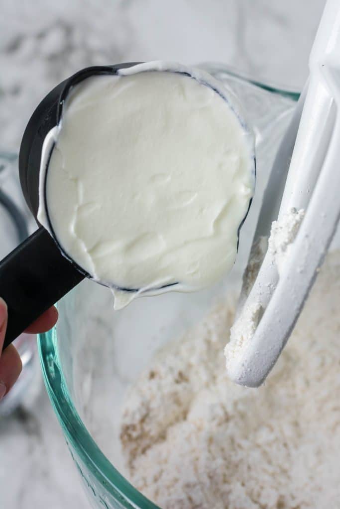 greek yogurt being added to a glass mixing bowl of English muffin dough