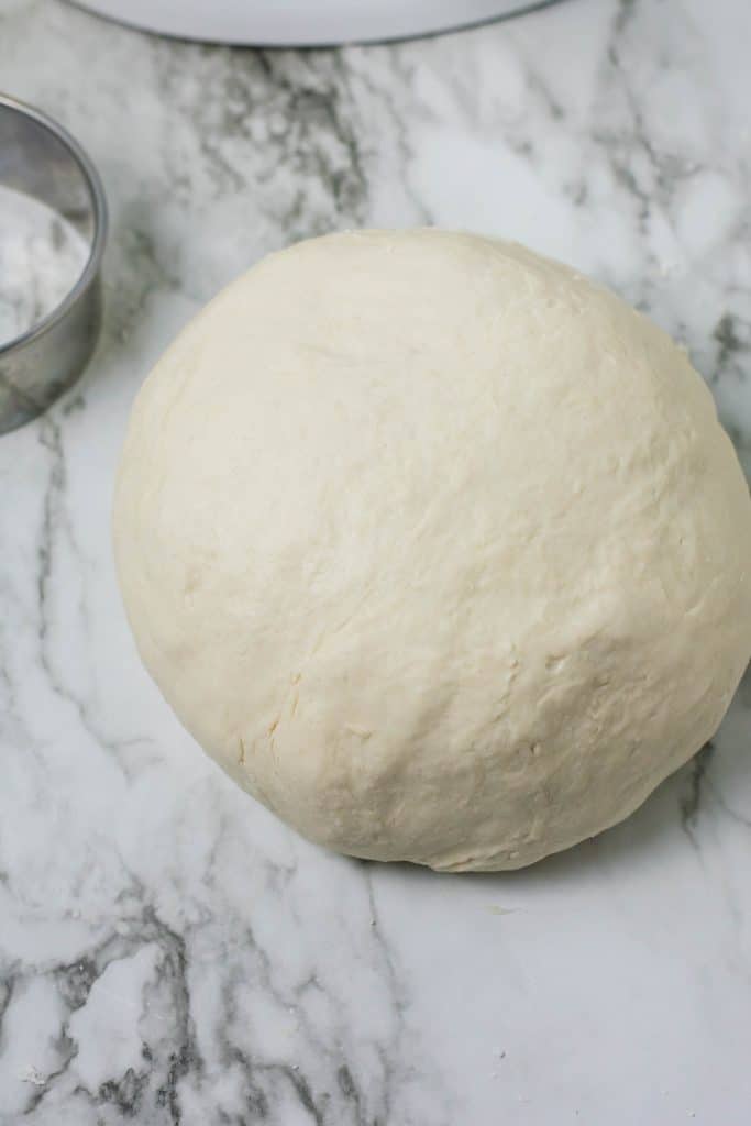 a ball of English muffin dough resting on a marble counter