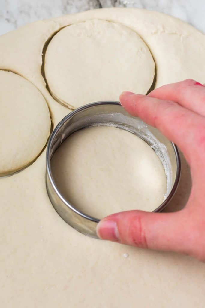 a round metal cutter cutting biscuits out of rolled out dough