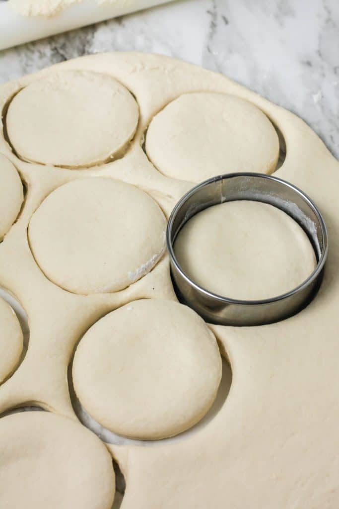 a round metal cutter cutting biscuits out of rolled out dough