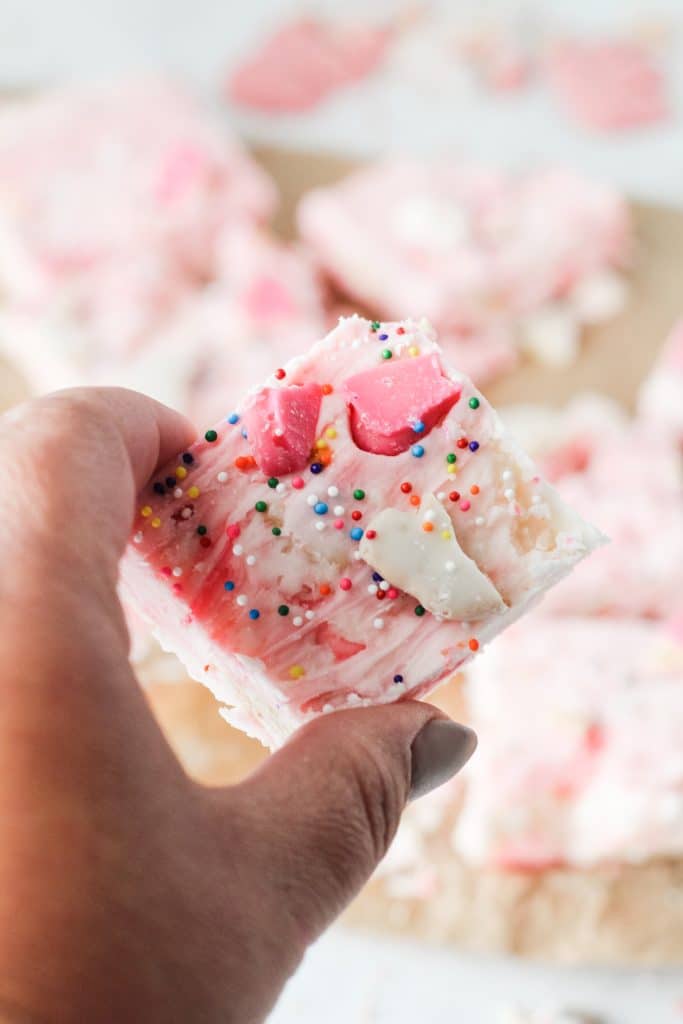 a hand holding up a square of pink circus cookie fudge