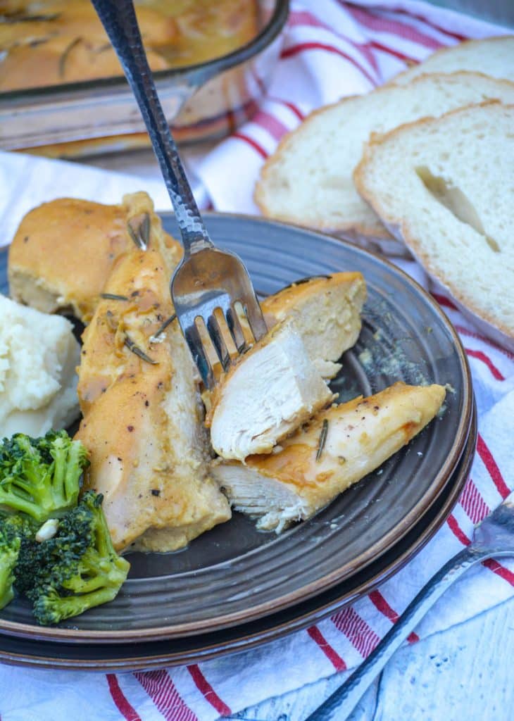 a fork stuck in a cut piece of rosemary dijon chicken on a brown dinner plate