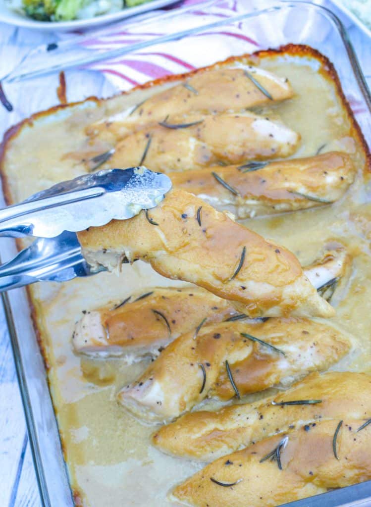 a pair of tongs holding up a slice of saucy rosemary dijon chicken