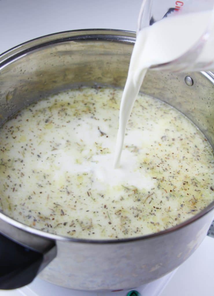 cream being poured into a silver pot of herbed chicken soup broth