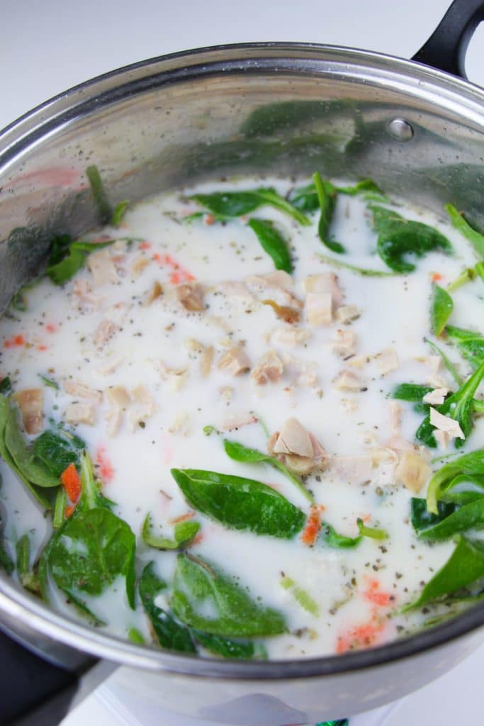 chicken, spinach, and carrots in a silver pot of creamy soup
