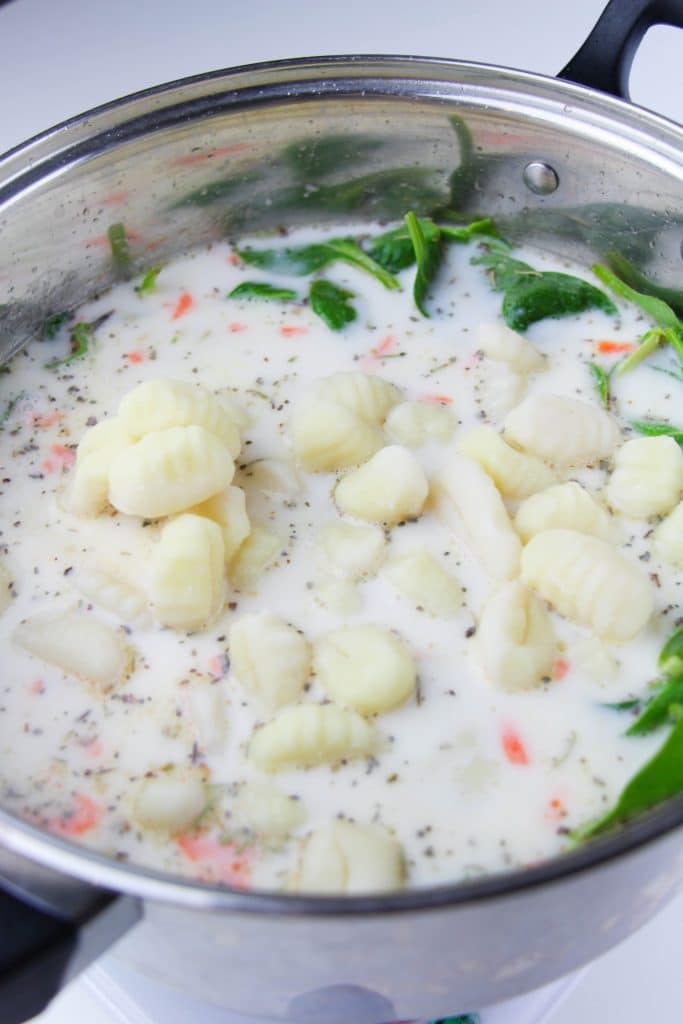 potato gnocchi being added to a silver pot of creamy chicken soup