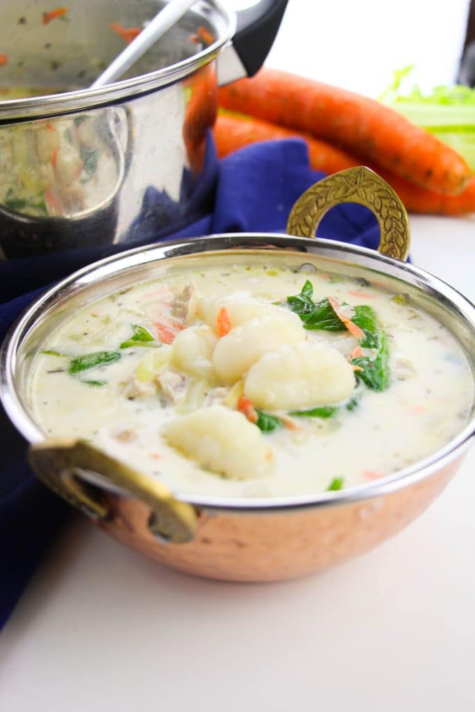 copycat olive garden chicken & gnocchi soup in a small bowl next to a silver pot