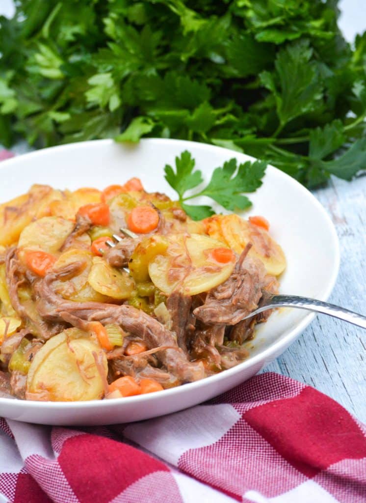 a silver fork digging into a white bowl filled with leftover pot roast casserole