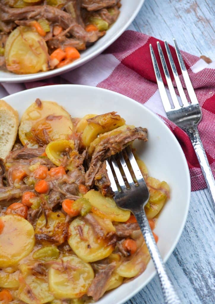 a silver fork digging into a white bowl filled with leftover pot roast casserole
