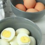 oven baked hard boiled eggs shown peeled & cut in half and piled in a gray bowl