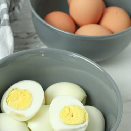 oven baked hard boiled eggs shown peeled & cut in half and piled in a gray bowl