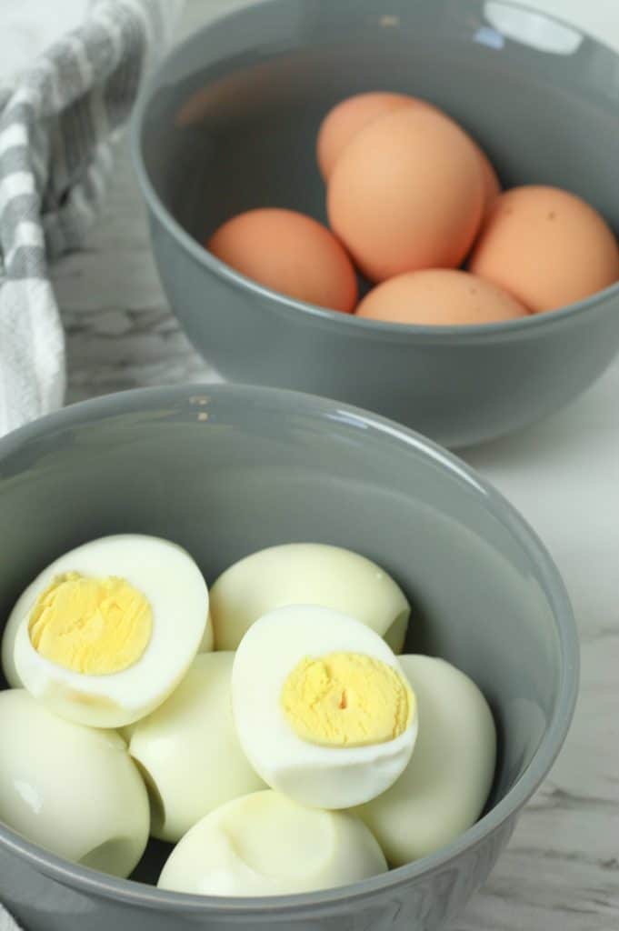 oven baked hard boiled eggs shown peeled & cut in half and piled in a gray bowl
