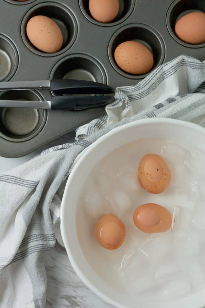 three baked hard boiled eggs shown in an ice bath in a white mixing bowl