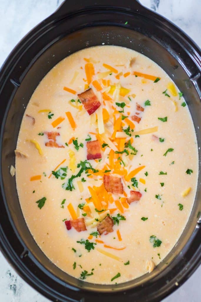 slow cooker crack chicken tortellini soup topped with shredded cheese, bacon pieces, and fresh parsley