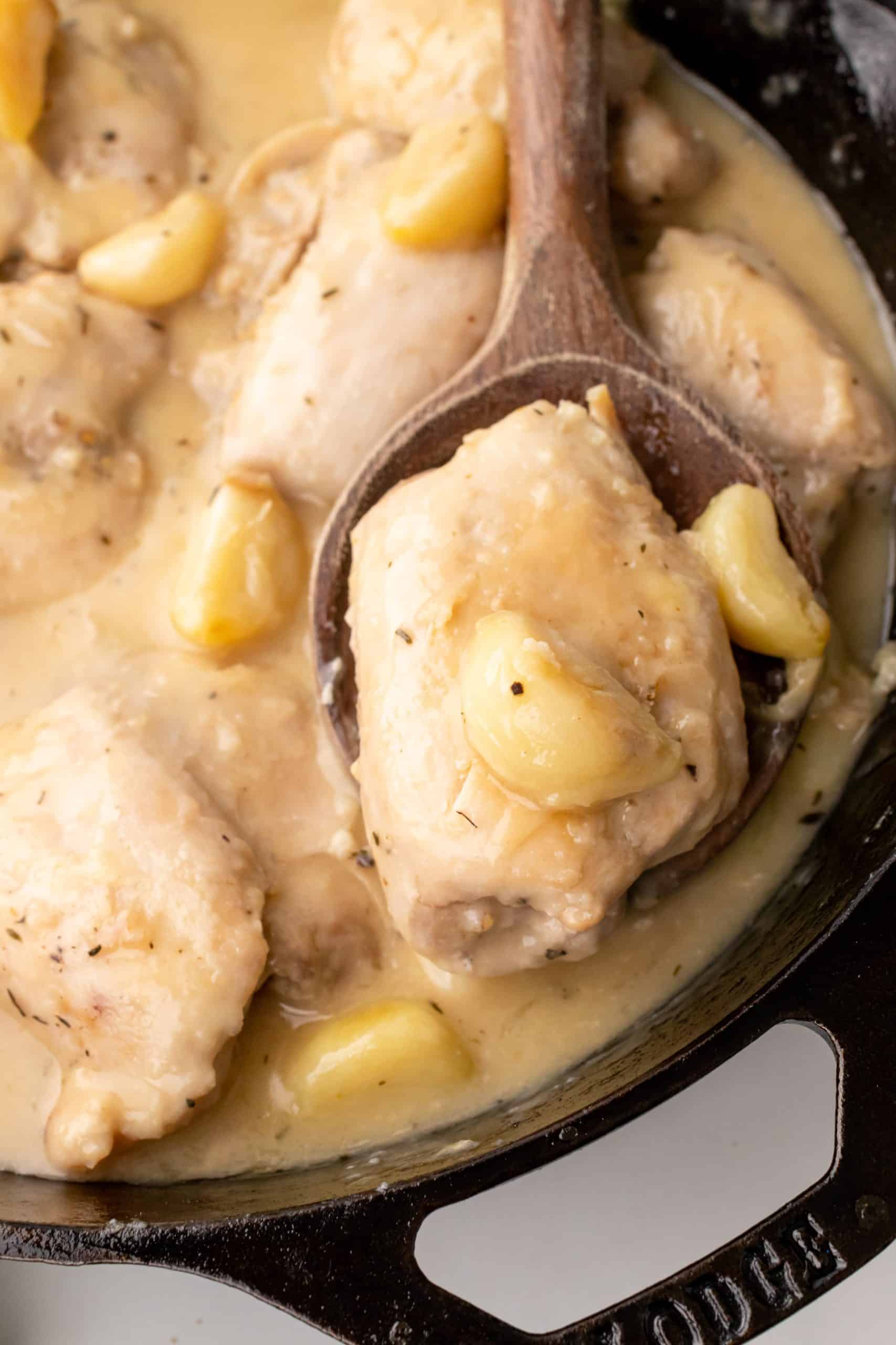 Pan Seared Chicken Thighs with Garlic Gravy a wooden spoon resting in a black skillet holding a chicken thigh in garlic gravy