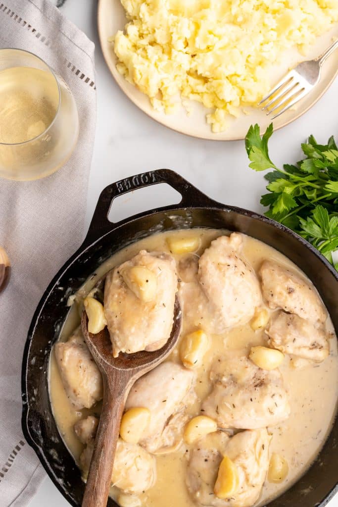 chicken thighs in garlic gravy in a black skillet with a wooden spoon
