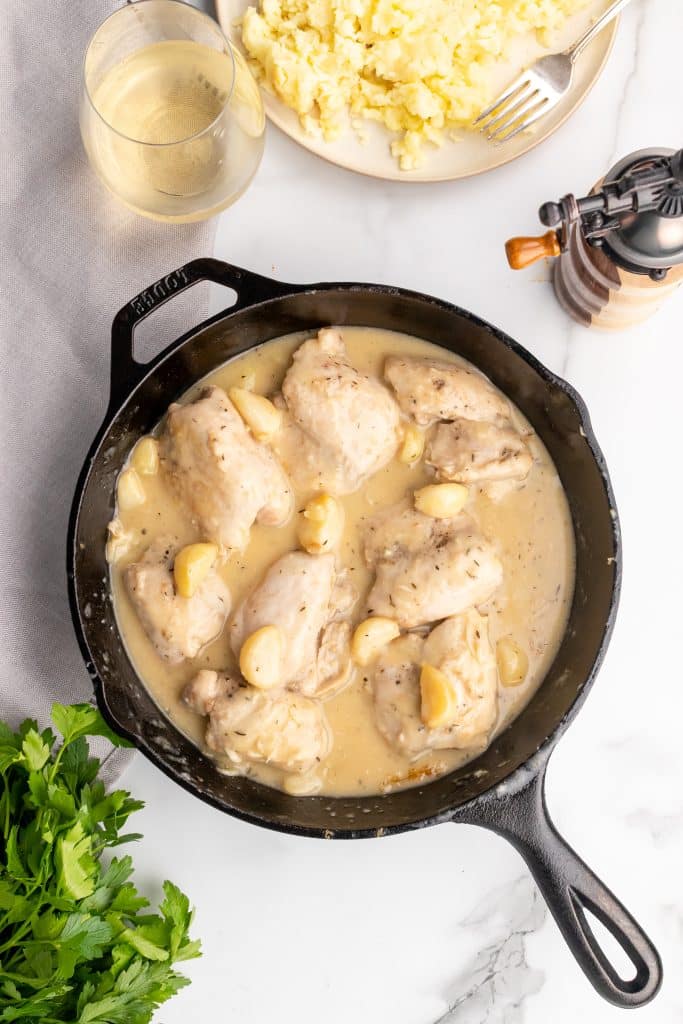 chicken thighs in garlic gravy in a black skillet with a wooden spoon
