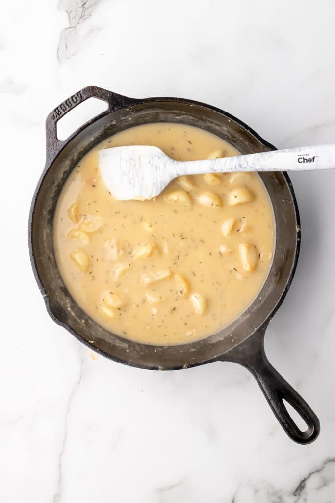 herbs and whole cloves in a brown garlic gravy in a black cast iron skillet