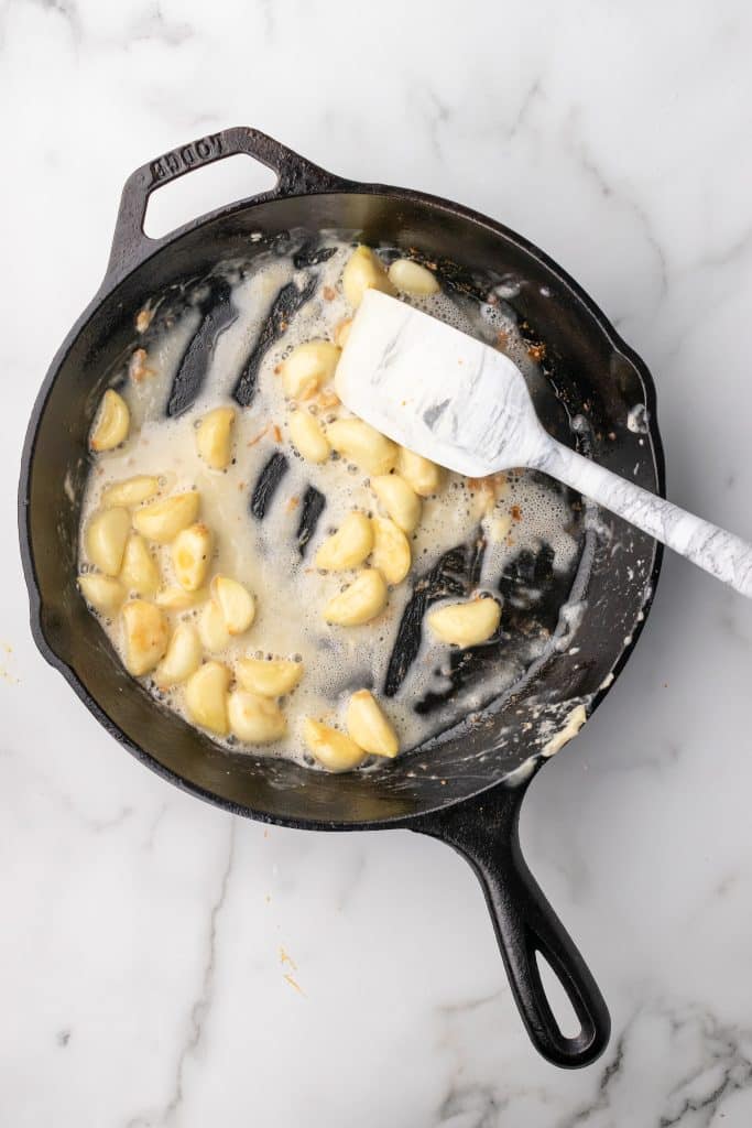 garlic cloves in a roux in a black cast iron skillet with a white spatula for stirring