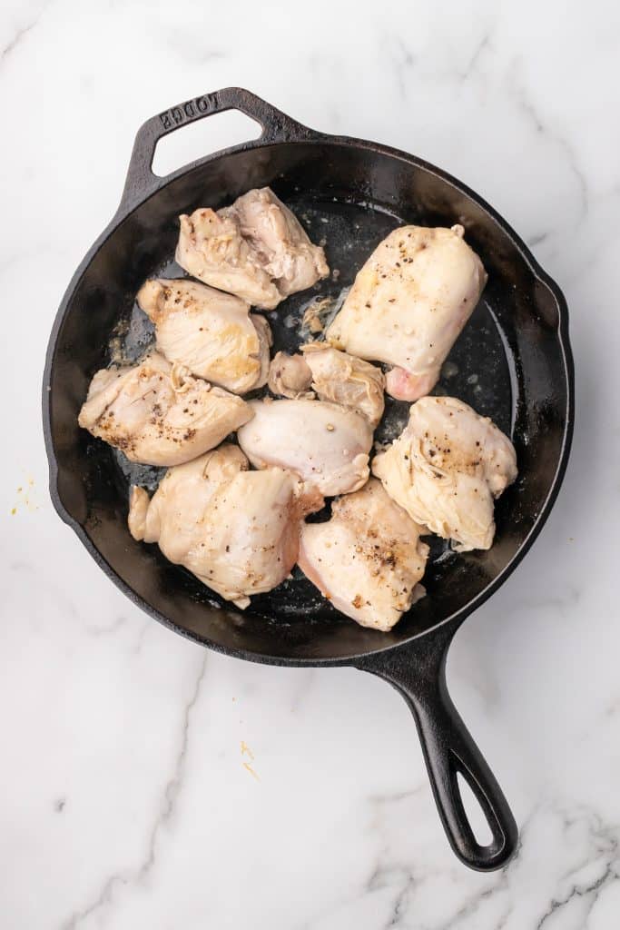 seasoned chicken thighs cooking in a black cast iron skillet