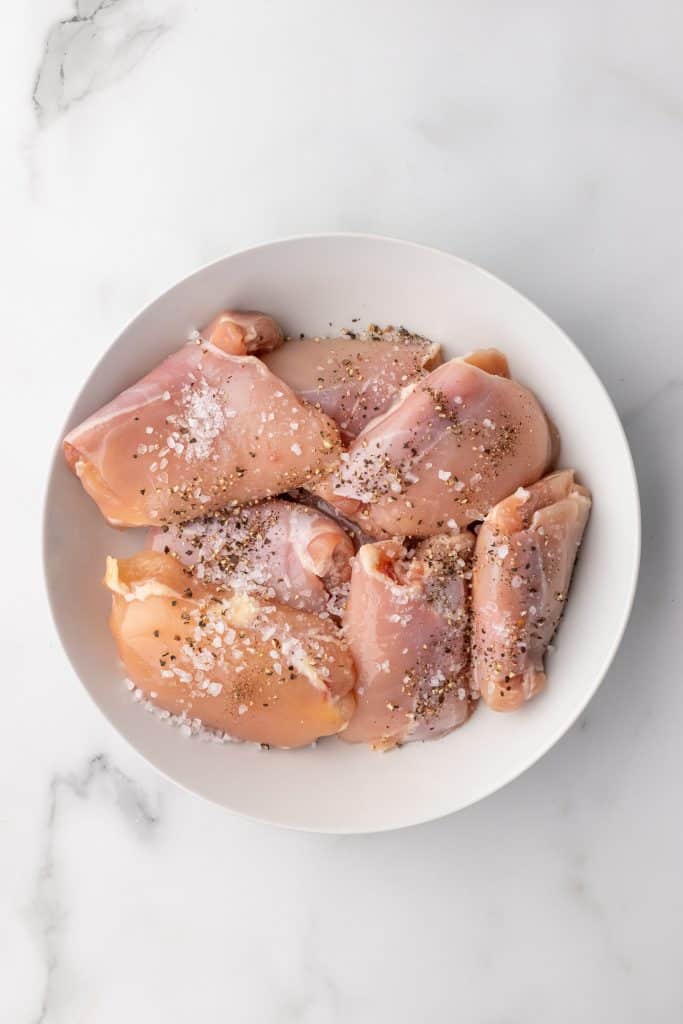 salt and pepper seasoned raw chicken thighs in a shallow white bowl