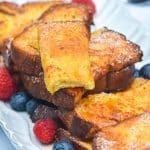 air fryer french toast sticks stacked on a white platter with berries