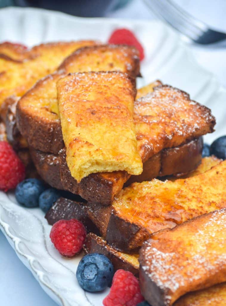 air fryer french toast sticks stacked on a white platter with berries
