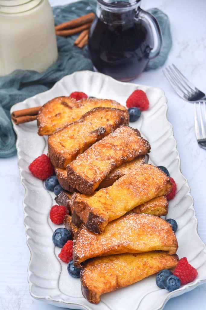 air fryer french toast sticks on a white platter surrounded by fresh berries