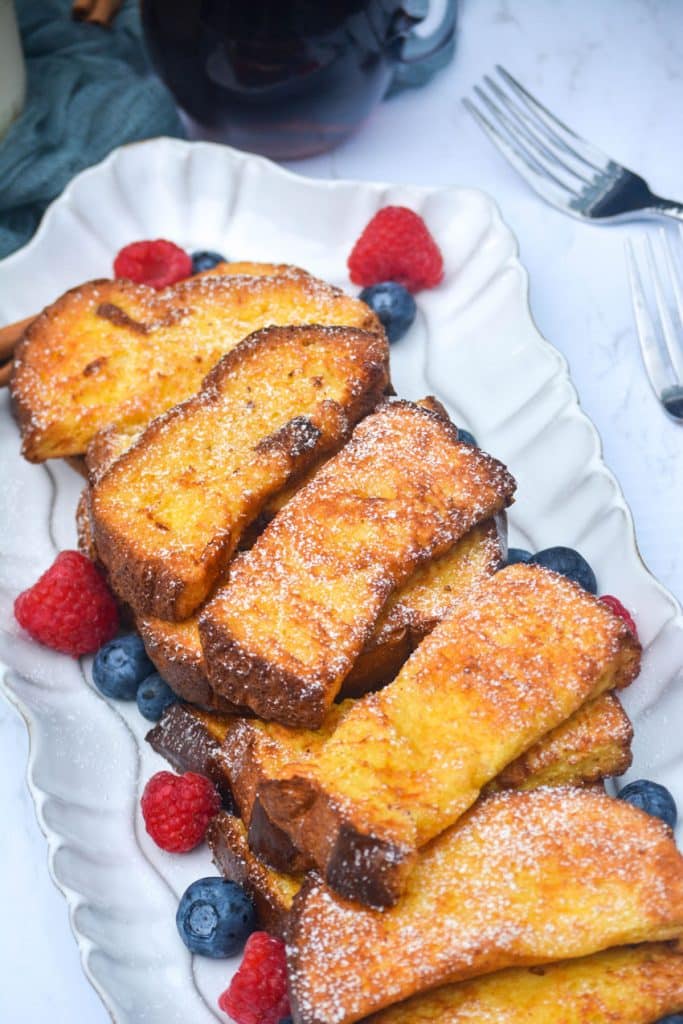 air fryer french toast sticks on a white platter surrounded by fresh berries