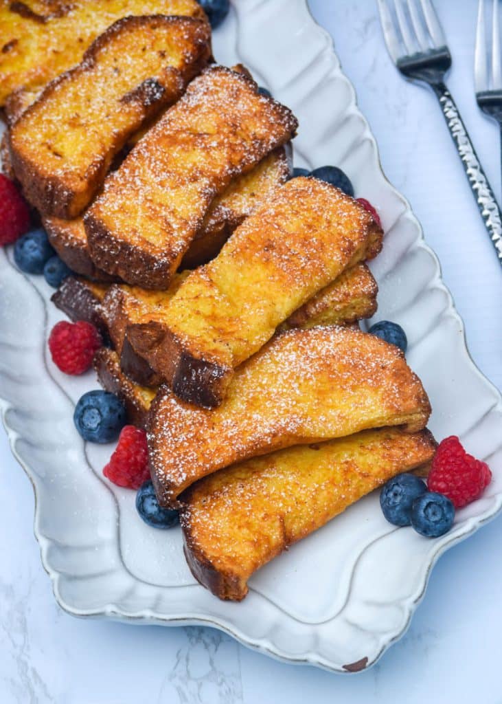 air fryer french toast sticks on a white platter surrounded by fresh berries