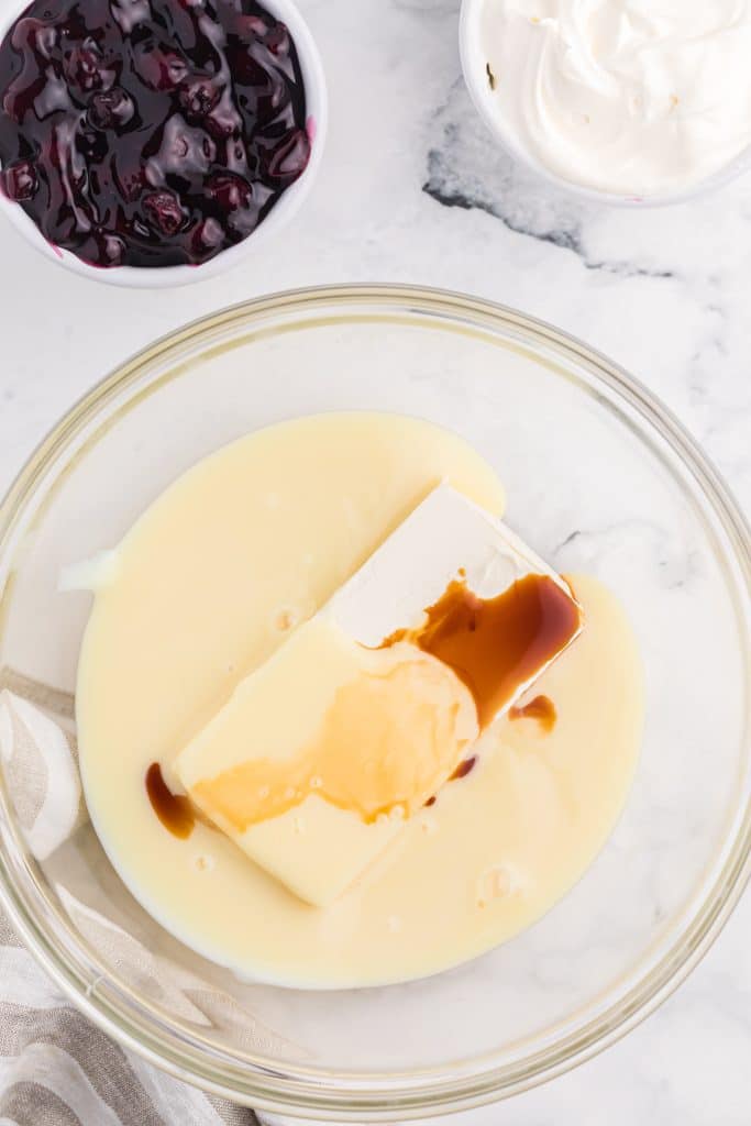 cheesecake batter ingredients in a large glass mixing bowl
